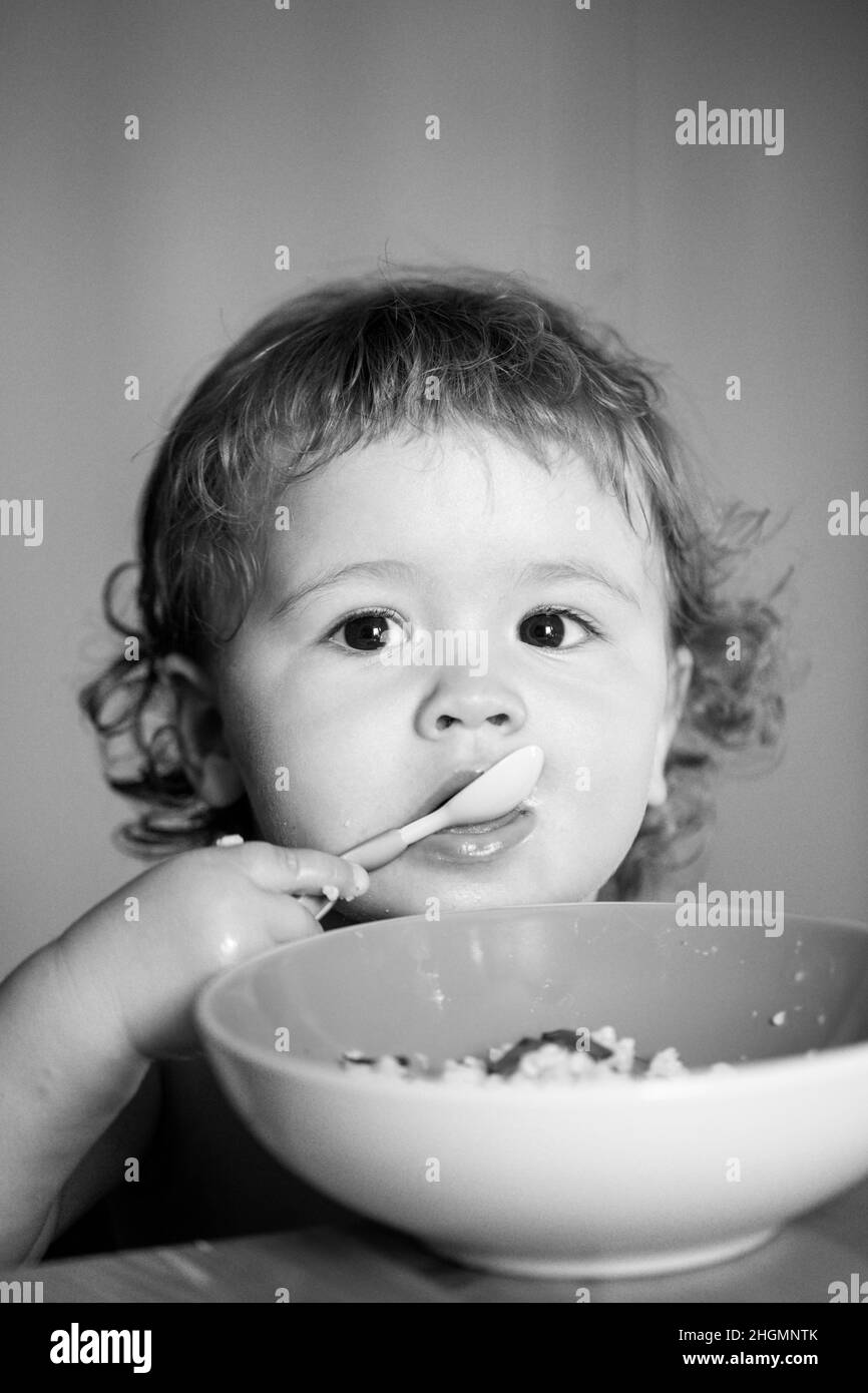 Funny baby eating food himself with a spoon on kitchen. Child nutrition ...
