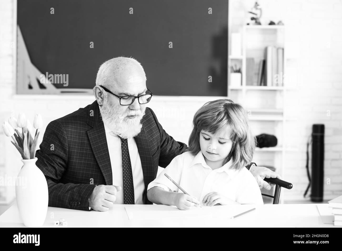 Old professor or senior teacher teaching little school boy. Educational conversation. Talking to students or pupils. School teacher concept. Stock Photo