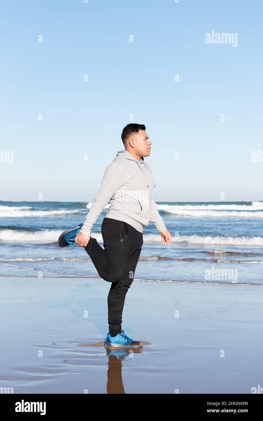 Young man stretching quadriceps muscle at the beach Stock Photo