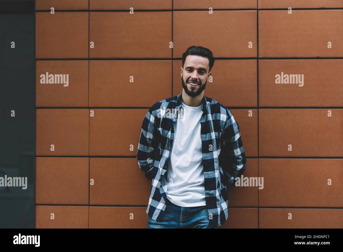 Half length portrait of joyful man in trendy clothing smiling at camera during free time in urban city Stock Photo