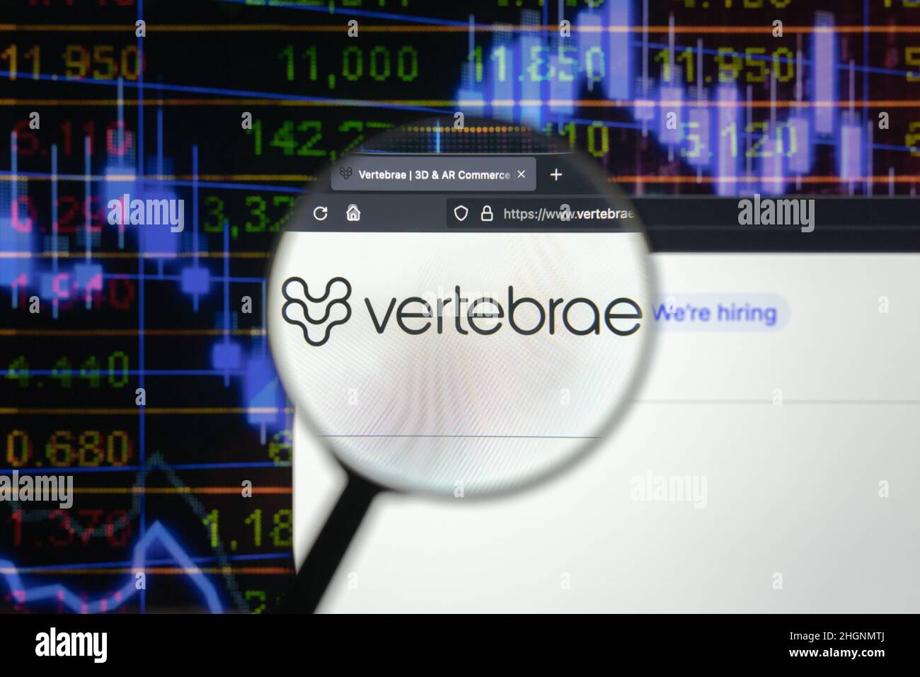 Vertebrae company logo on a website with blurry stock market developments in the background, seen on a computer screen through a magnifying glass. Stock Photo