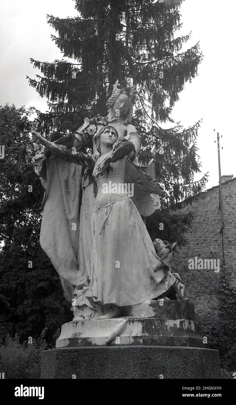 1950s, historical, A statue in front of La Maison Natale de Jeanne d'Arc, a two-storey stone farm building, with sloping roof, where Joan of Arc was born in the 15th century, Domremy-la-Pucelle, France.  Her birth house in Domrémy was preserved and became a museum. Also known as the 'The Maid of Orleans' this simple peasant girl is considered a national heroine in French culture, as believing that she was acting under the will of god, she led the French army to victory at Orleans in 1429 against the English during the Hundred Years War. Stock Photo