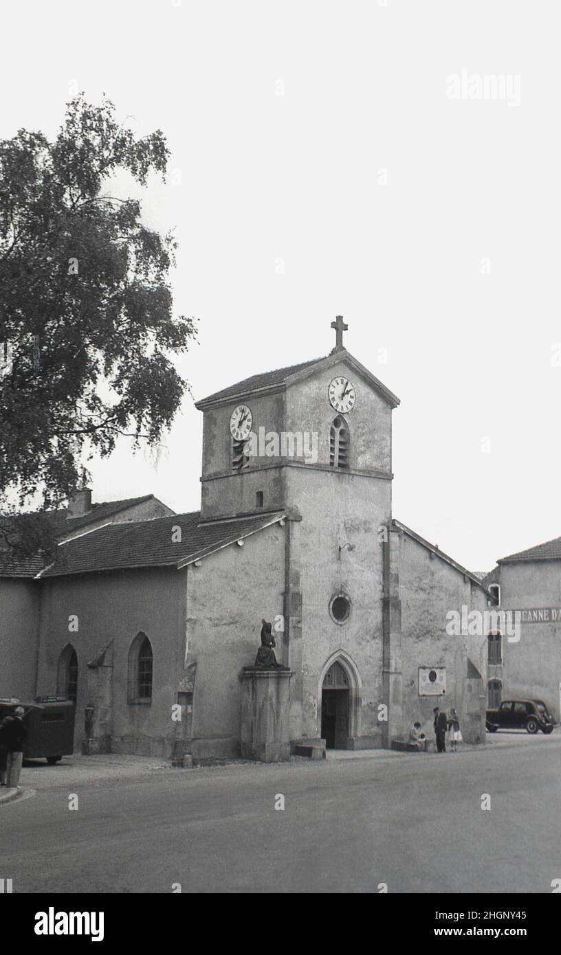 1950s, historical, the 13th century church in the village of Domremy, France and home of La Maison Natale De Jeanne d'Arc, the birth house of French national heroine. Next door to the church, Hotel de Jeanne d'Arc. The village church is where Joan of Arc attended Mass. Also known as the 'The Maid of Orleans' this simple peasant girl is considered a national heroine in French culture, as believing that she was acting under the will of god, she led the French army to victory at Orleans in 1429 against the English during the Hundred Years War. Stock Photo