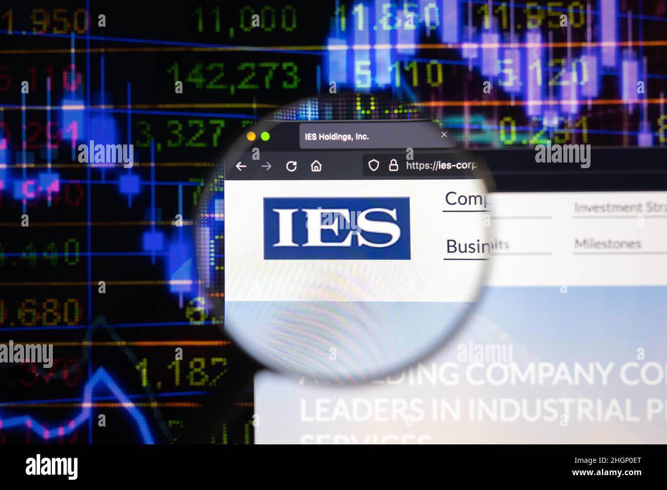 IES company logo on a website with blurry stock market developments in the background, seen on a computer screen through a magnifying glass. Stock Photo