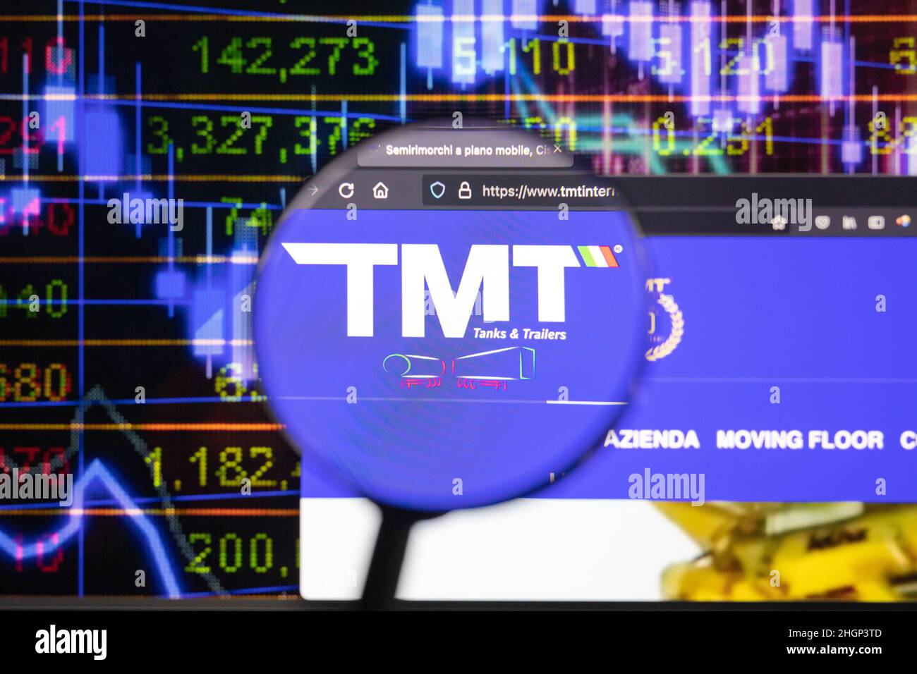 TMT company logo on a website with blurry stock market developments in the background, seen on a computer screen through a magnifying glass. Stock Photo