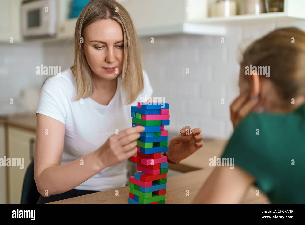 Woman and daughter playing jenga tower game at home. Stock Photo