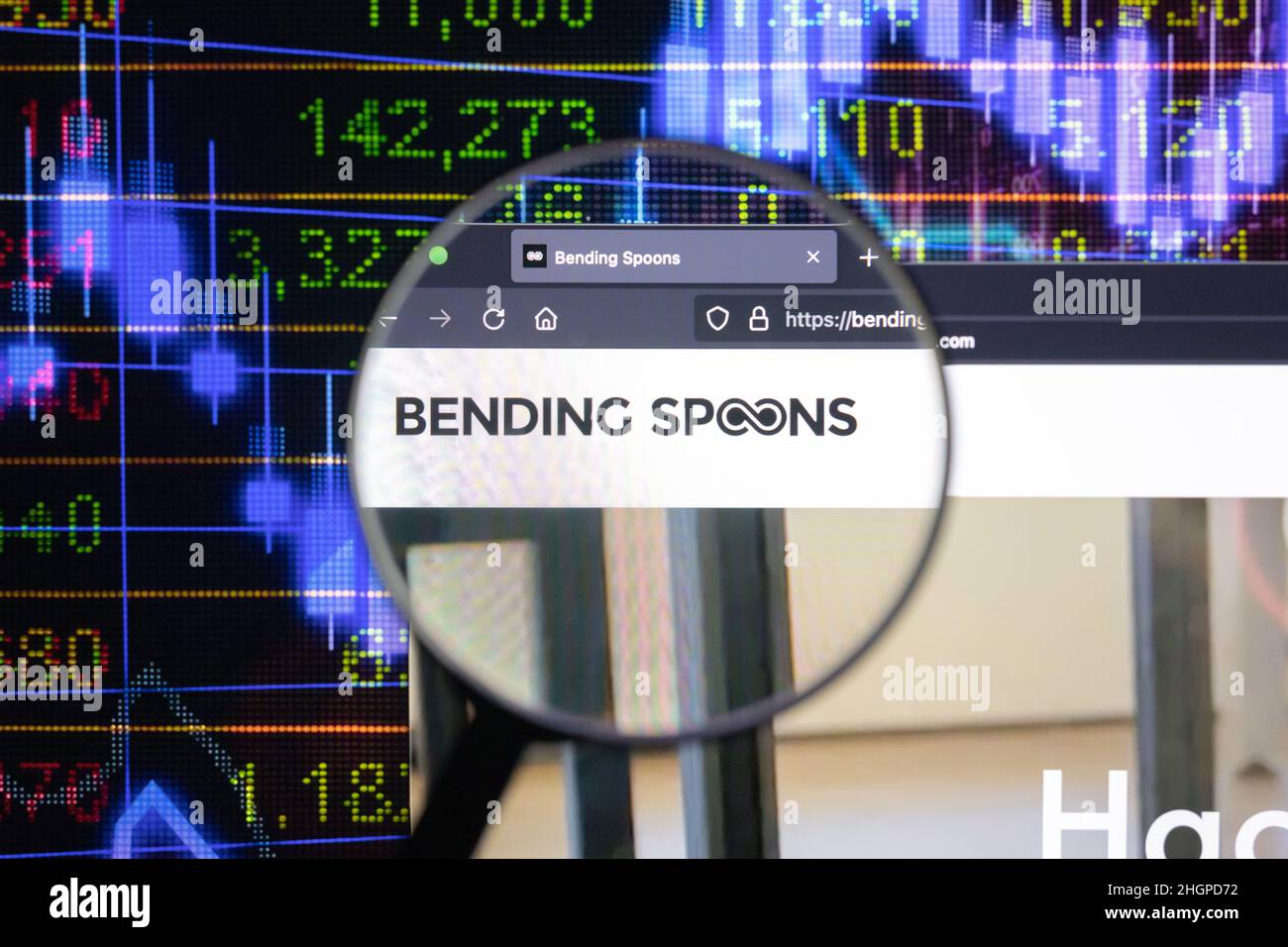Bending Spoons company logo on a website with blurry stock market developments in the background, seen on a computer screen through a magnifying glass Stock Photo