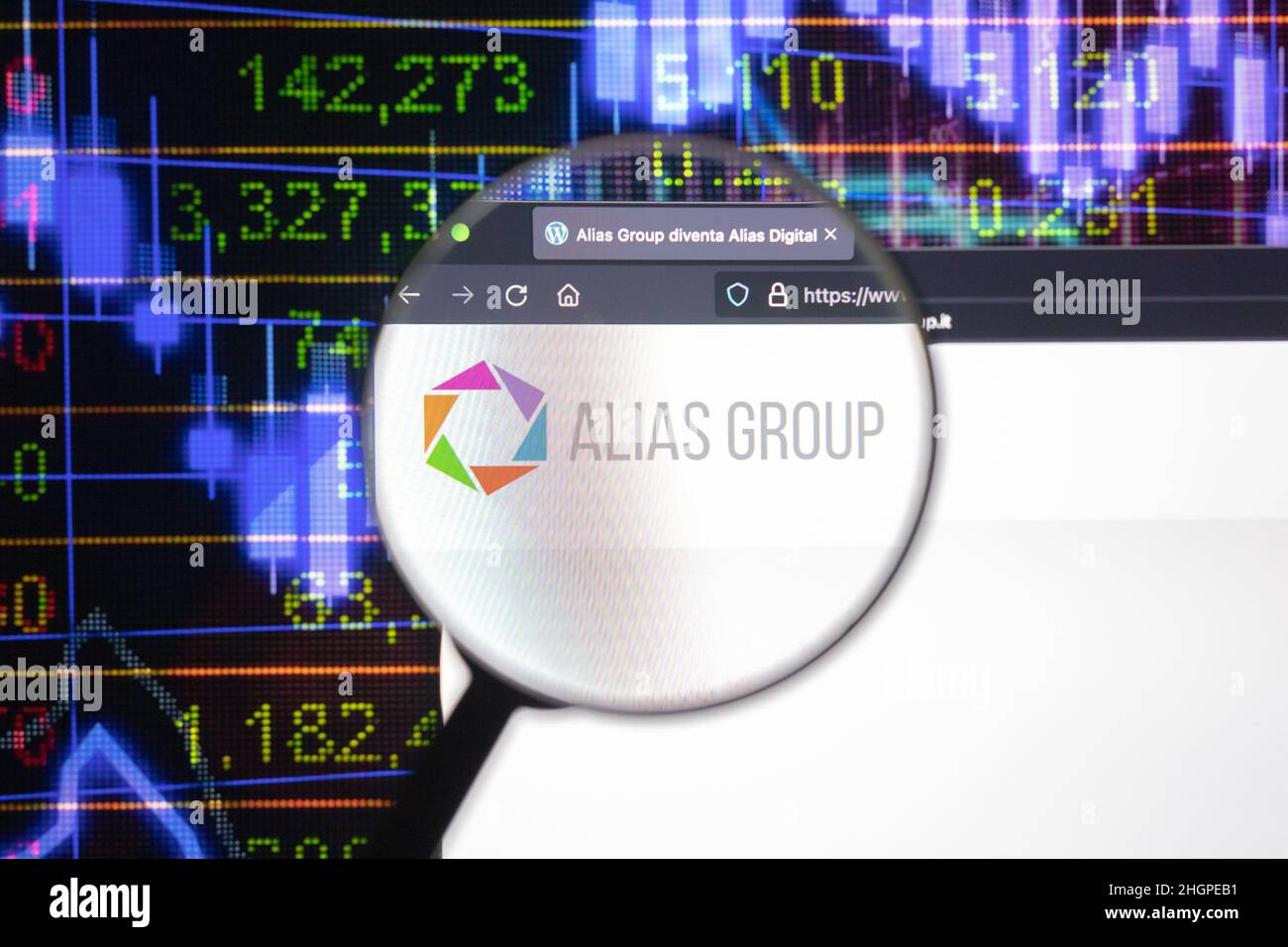 Alias Group company logo on a website with blurry stock market developments in the background, seen on a computer screen through a magnifying glass. Stock Photo