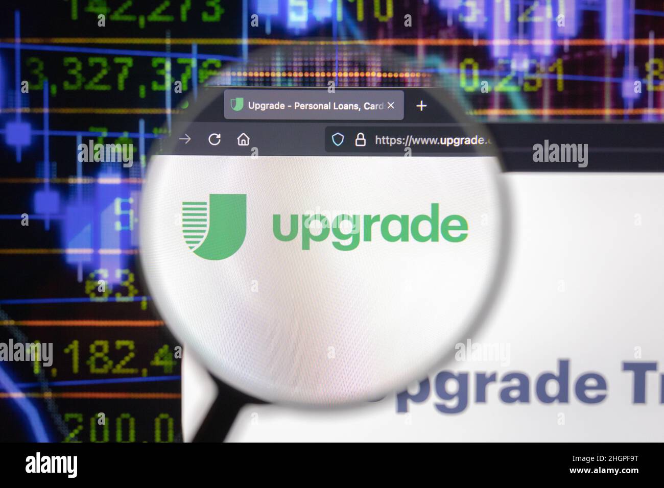 Upgrade company logo on a website with blurry stock market developments in the background, seen on a computer screen through a magnifying glass. Stock Photo