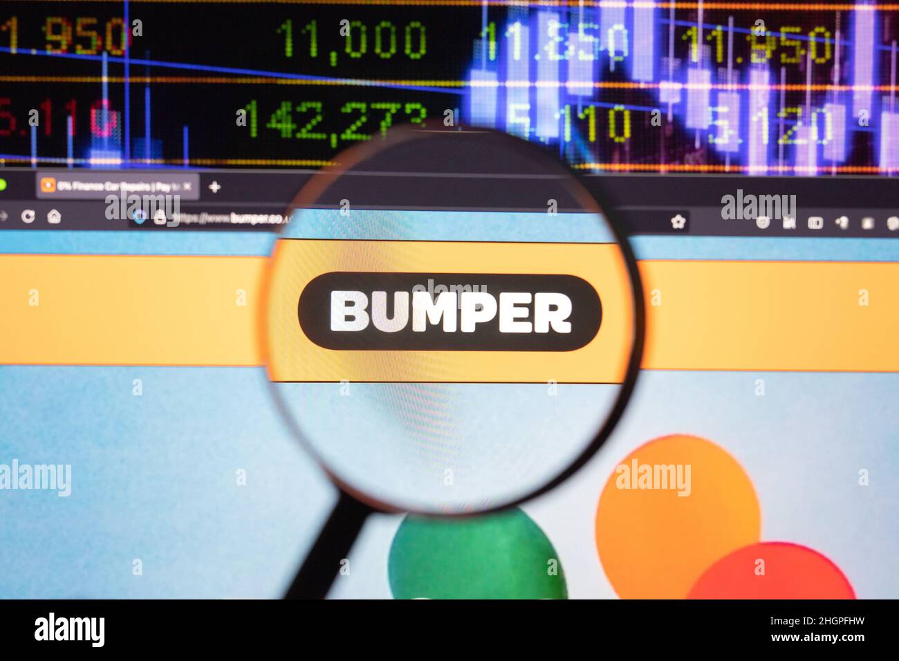Bumper company logo on a website with blurry stock market developments in the background, seen on a computer screen through a magnifying glass. Stock Photo