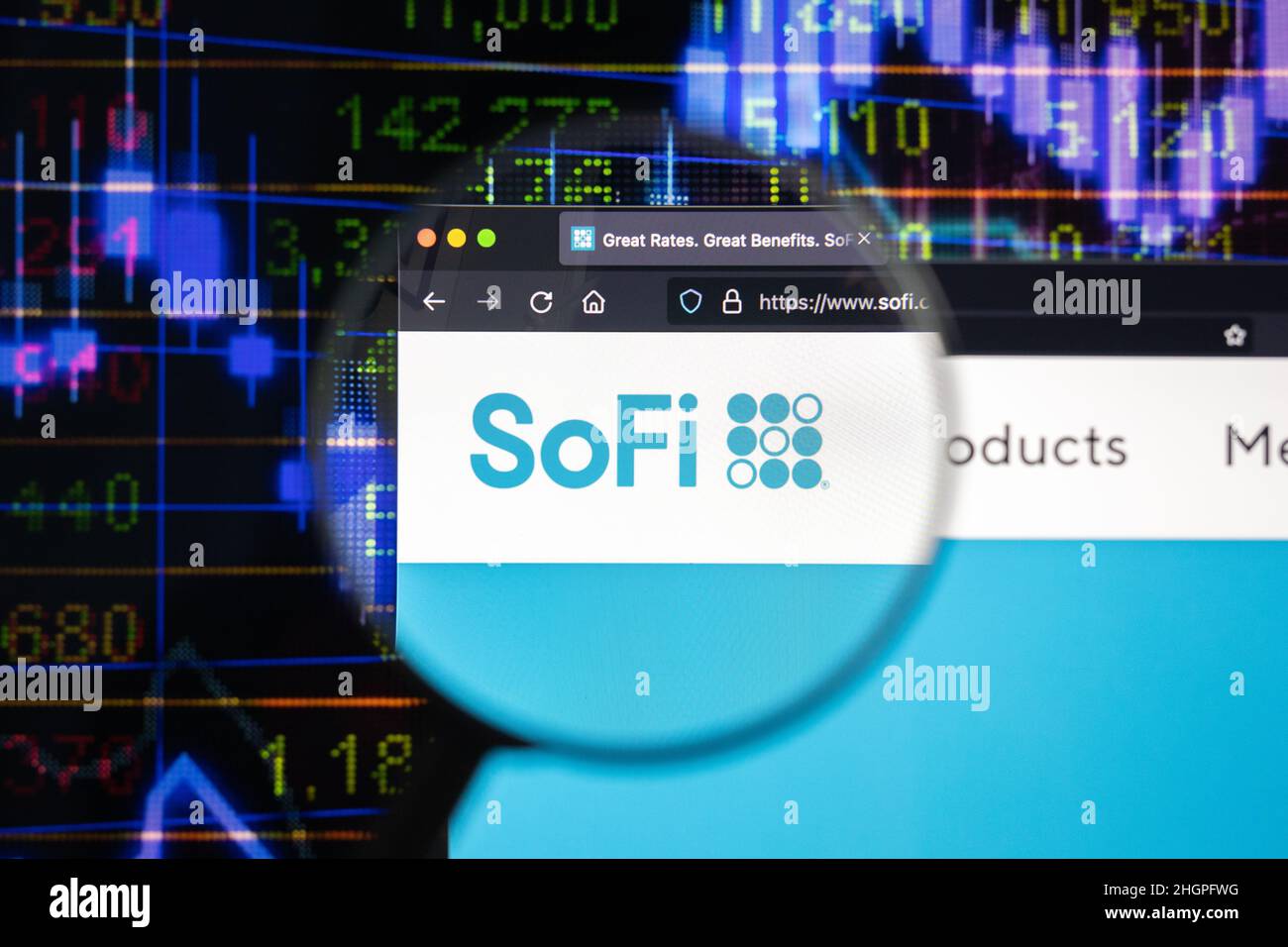SoFi company logo on a website with blurry stock market developments in the background, seen on a computer screen through a magnifying glass. Stock Photo