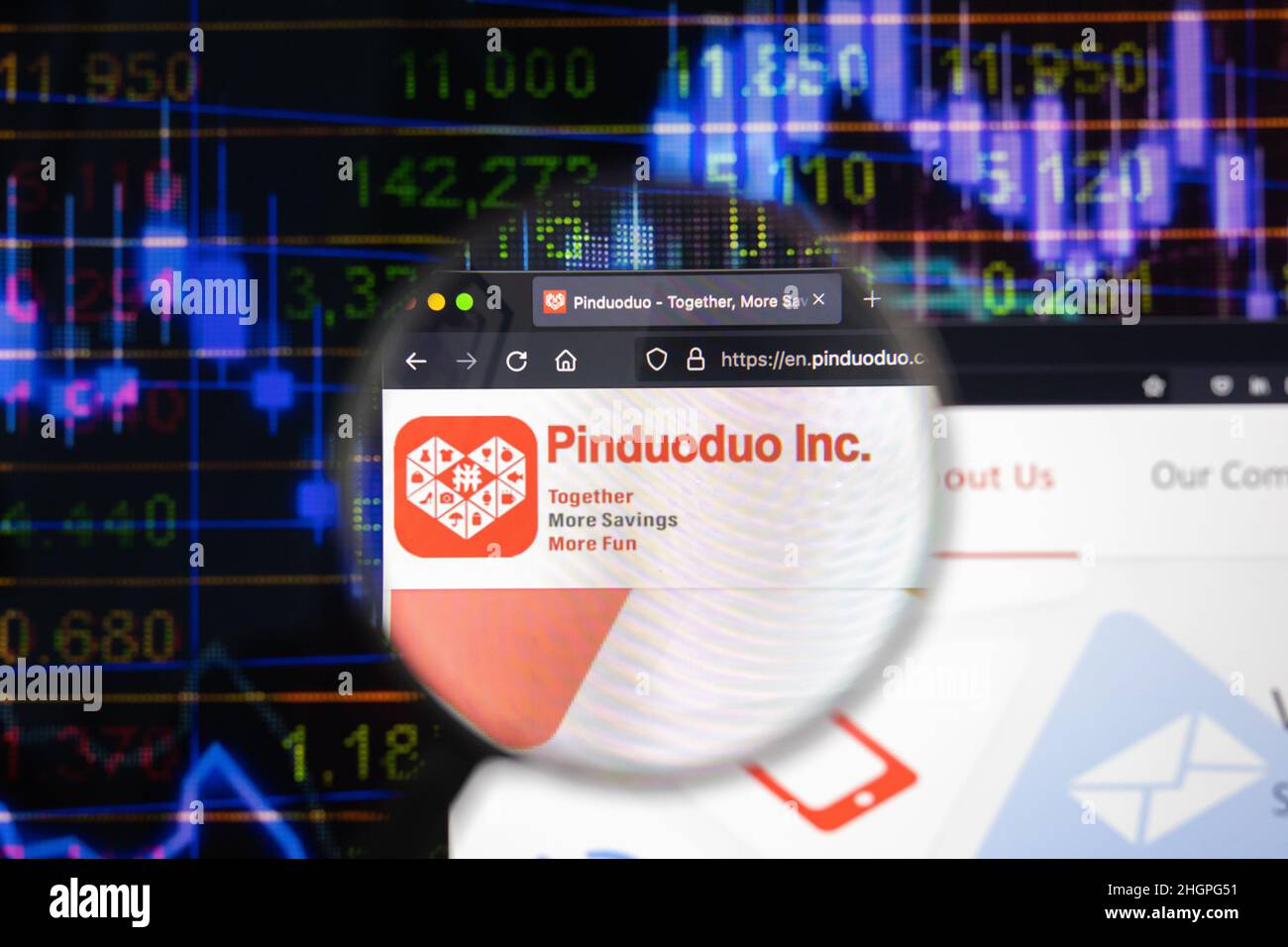 Pinduoduo Inc. company logo on a website with blurry stock market developments in the background, seen on a computer screen through a magnifying glass Stock Photo