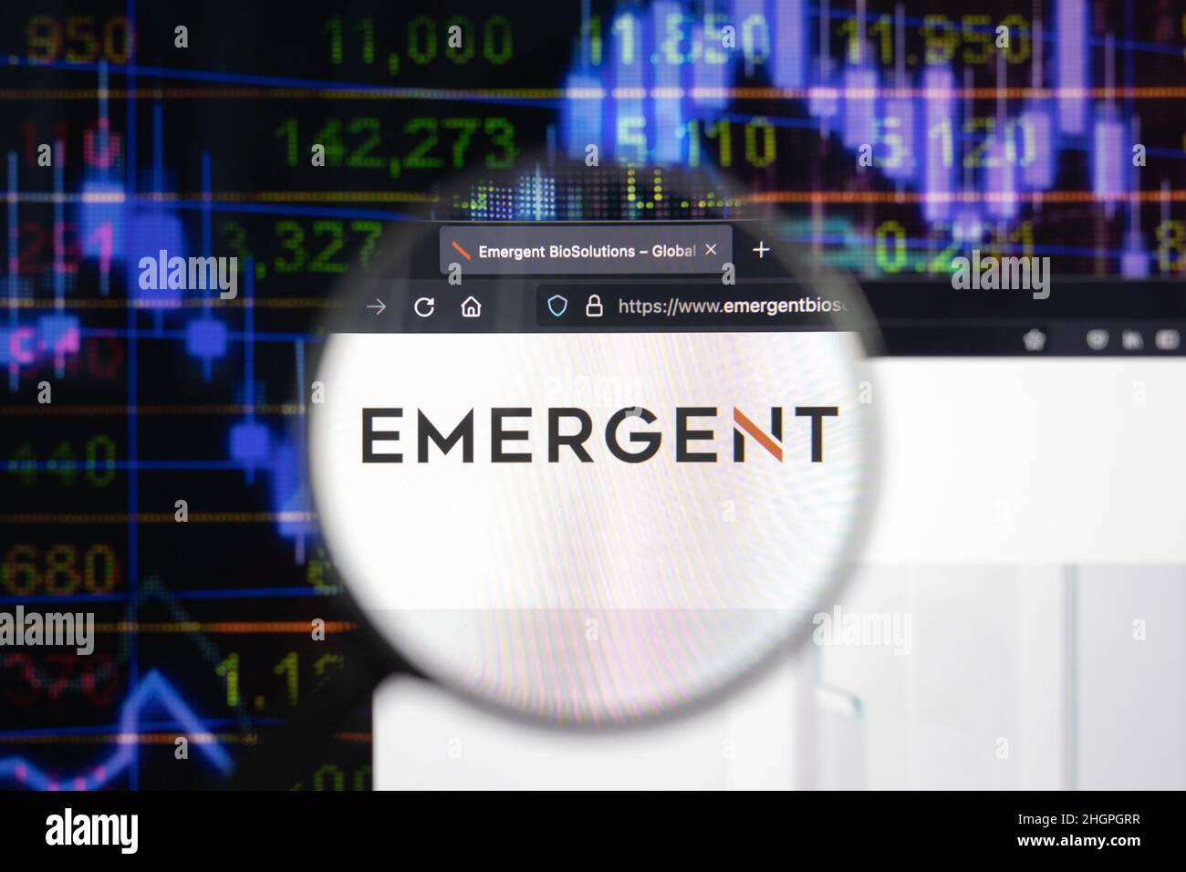 Emergent company logo on a website with blurry stock market developments in the background, seen on a computer screen through a magnifying glass. Stock Photo
