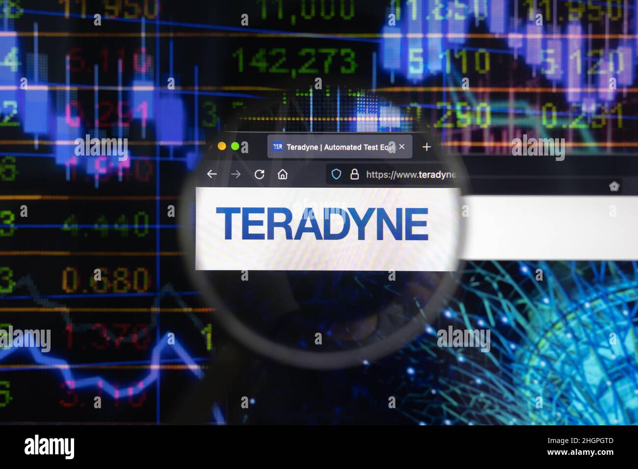 Teradyne company logo on a website with blurry stock market developments in the background, seen on a computer screen through a magnifying glass. Stock Photo