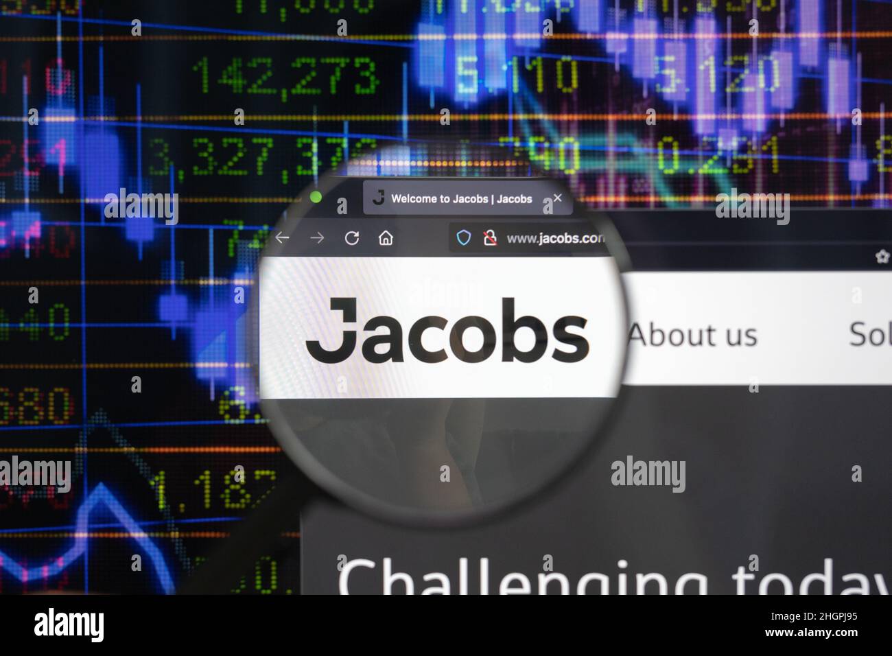 Jacobs company logo on a website with blurry stock market developments in the background, seen on a computer screen through a magnifying glass. Stock Photo