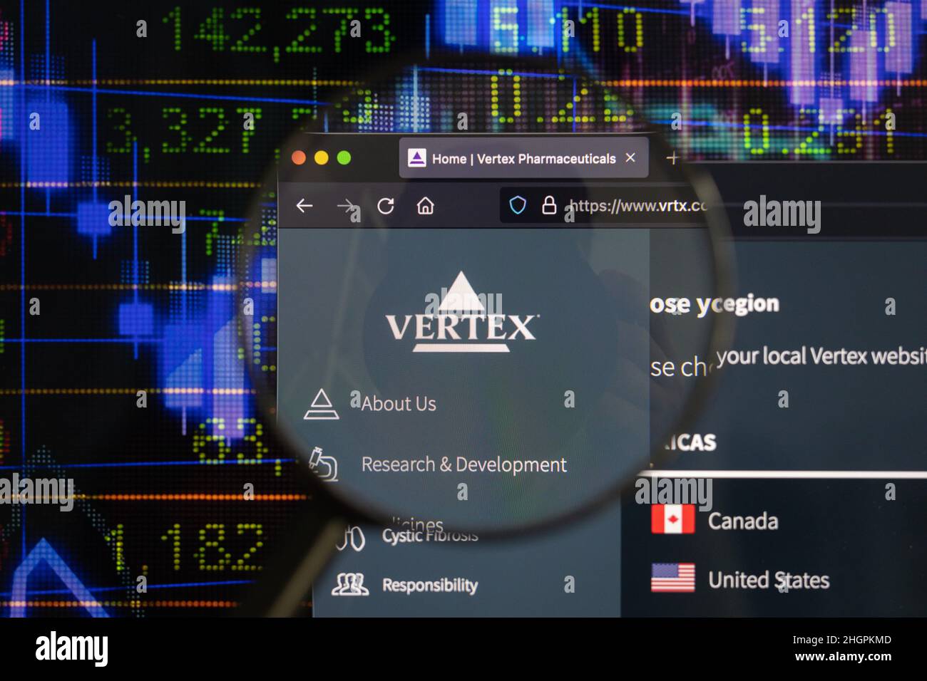 Vertex company logo on a website with blurry stock market developments in the background, seen on a computer screen through a magnifying glass. Stock Photo