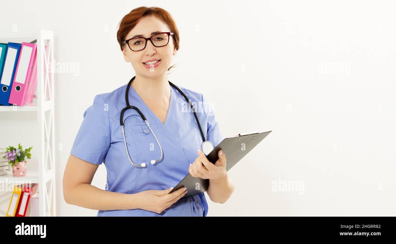 Beautiful smiling female doctor stands in medical office and shows like. Health care concept, medical insurance, Copy space. Stock Photo