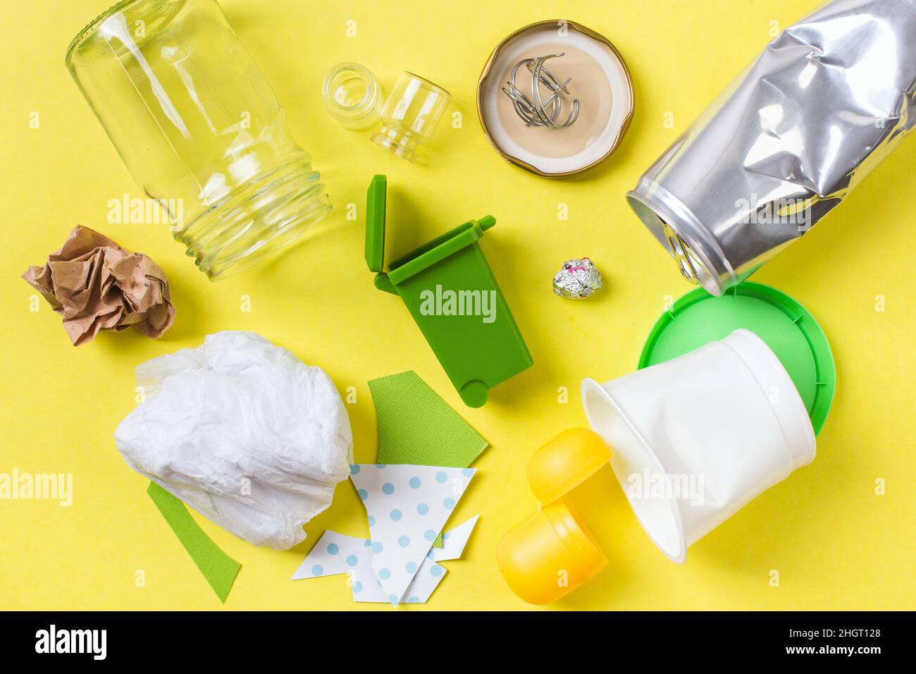 Clean trash to recycle in small bin metal, plastic paper and glass. Recycling concept on yellow. Stock Photo