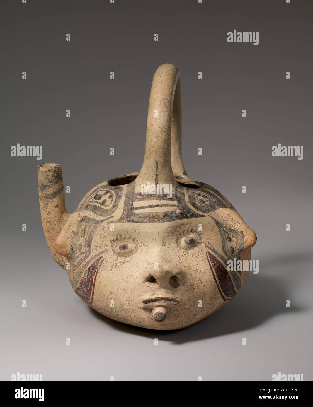 Spouted Vessel 13th–15th century Huastec The vessel is in the shape of a human head with wide open, staring eyes, a small pug nose, and closed mouth. A lip plug is worn in the lower lip. A handle extends from the forehead to the back of the head. On the right side behind the ear projects a single spout pointing upward. On the sides of the face and back of the head the cream-colored surface is covered with geometric motifs including dots, circles, diamonds and crosses in dark brown and purple.. Spouted Vessel. Huastec. 13th–15th century. Ceramic. Mexico, Mesoamerica, Veracruz. Ceramics-Containe Stock Photo