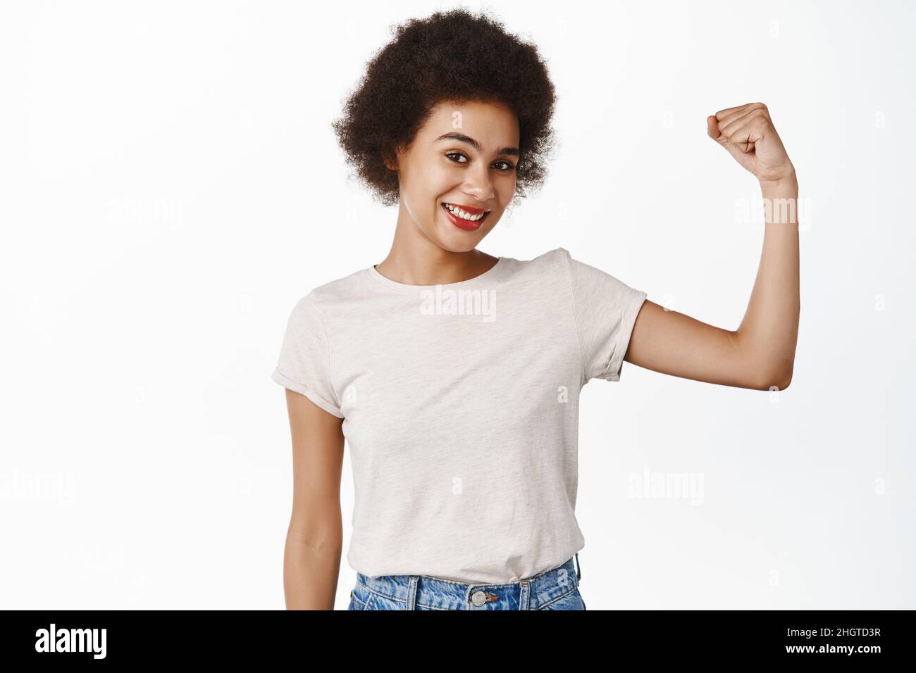 Strength and women workout concept. Smiling black girl with afro hair, young woman flexing biceps, showing muscles on arms, standing over white Stock Photo