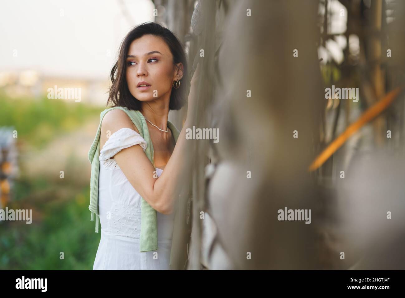 Asian woman, posing near a tobacco drying shed, wearing a white dress and green wellies. Stock Photo