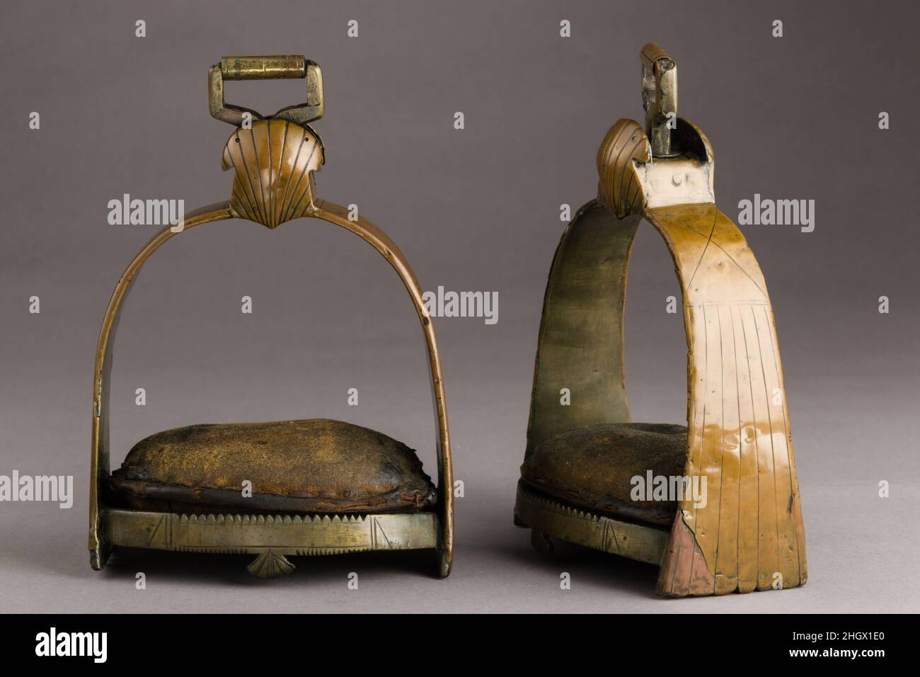 Pair of Stirrups 17th century German The large size of these stirrups is unusual for the period. They may have been used by a postilion, a driver riding one of the carriage horses. However stirrups for this purpose typically had simpler designs. Indeed, to prevent their legs being crushed between the two horses or the central wooden shaft, postilion riders wore heavy oversized reinforced boots, and they consequently needed larger spurs and stirrups. The small leather cushions are also unusual, and may be later additions.. Pair of Stirrups. German. 17th century. Iron, copper alloy, leather. Equ Stock Photo