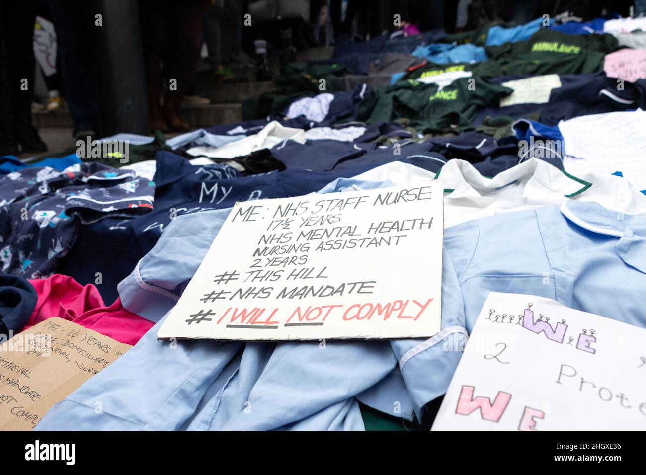 A placard placed on top of NHS uniforms, that says 'Me: NHS staff nurse for 17.5 years. NHS mental health nursing assistant for 2 years. This hill NHS mandate. I will not comply' during the demonstration.By April 2022, 100k members of the NHS will have to be fully vaccinated or lose their jobs. In light of this draconian requirement, NHS nurses have come together to protest against such coercion, defending their medical freedom and accusing the government for a total mistreatment of the health workers over the pandemic. Other anti-lockdown and anti-vaccine groups have jointly protested against Stock Photo