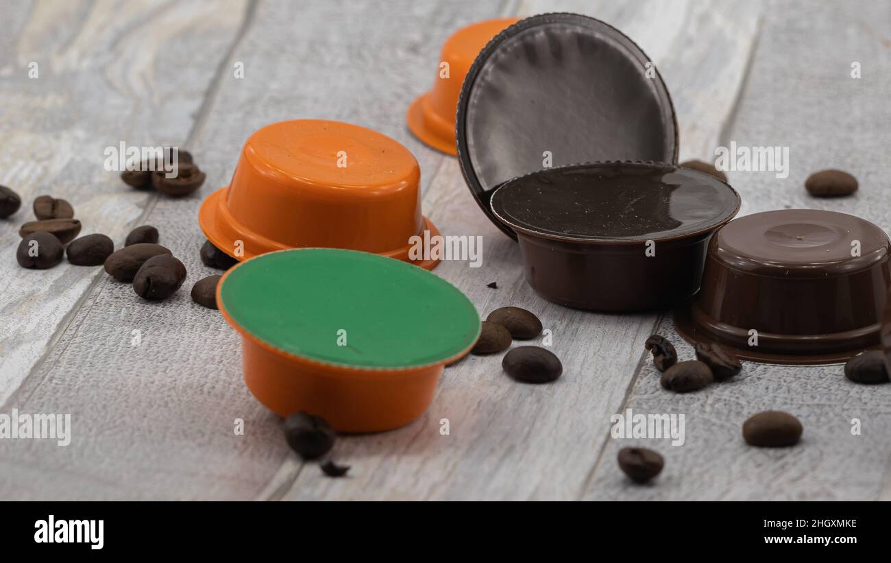 coffee capsules and coffee beans scattered on a light wooden surface Stock Photo