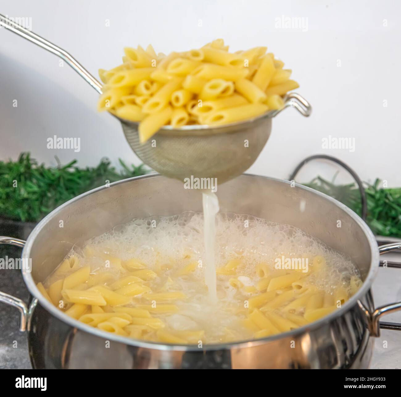 Cooking Pasta pour the penne pasta into a metal pot of boiling water