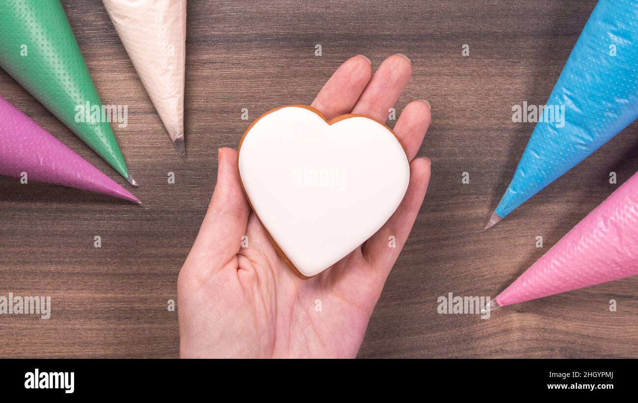 Hand holding white heart shape cookie for Mothers day, Womans day or Valentines Day on wooden background. Copy space Stock Photo