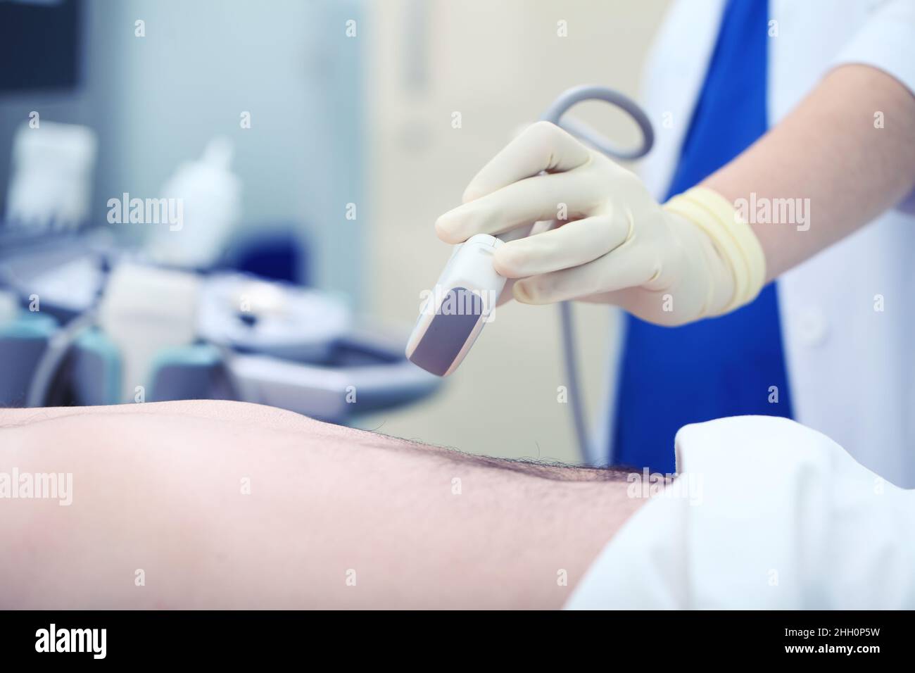 Female doctor in the work wear holds with gloved hands ultrasound device over the male patient body. Stock Photo