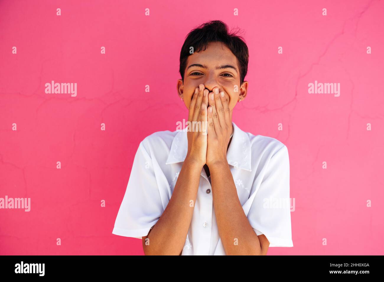 Cheerful queer boy coming out and embracing his identity. Happy gay teenager covering his mouth with his hands while smiling. Young teenage boy standi Stock Photo