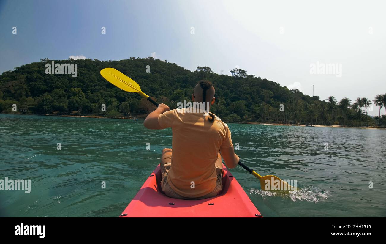 Man with sunglasses and hat rows pink plastic canoe along sea ag Stock Photo