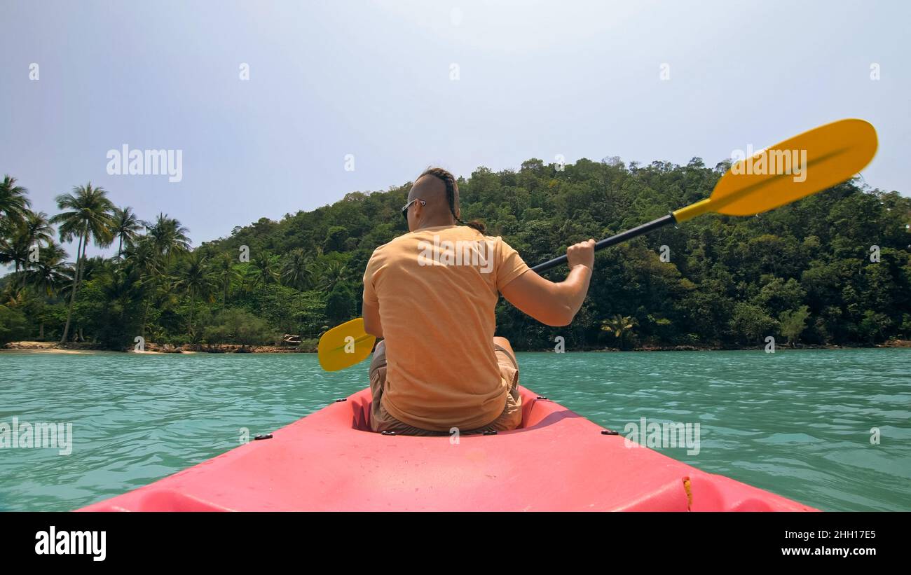 Man with sunglasses and hat rows pink plastic canoe along sea ag Stock Photo