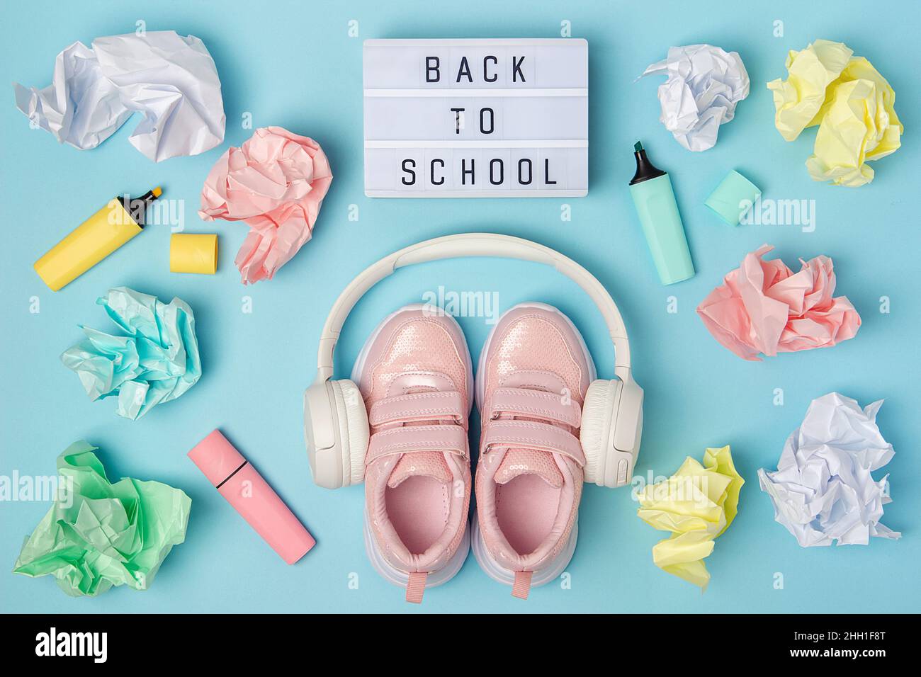 Back to school text on lightbox. Headphones, pink shoes, colored crumpled paper balls, marker on blue background. Education concept. Flatlay Top view Stock Photo