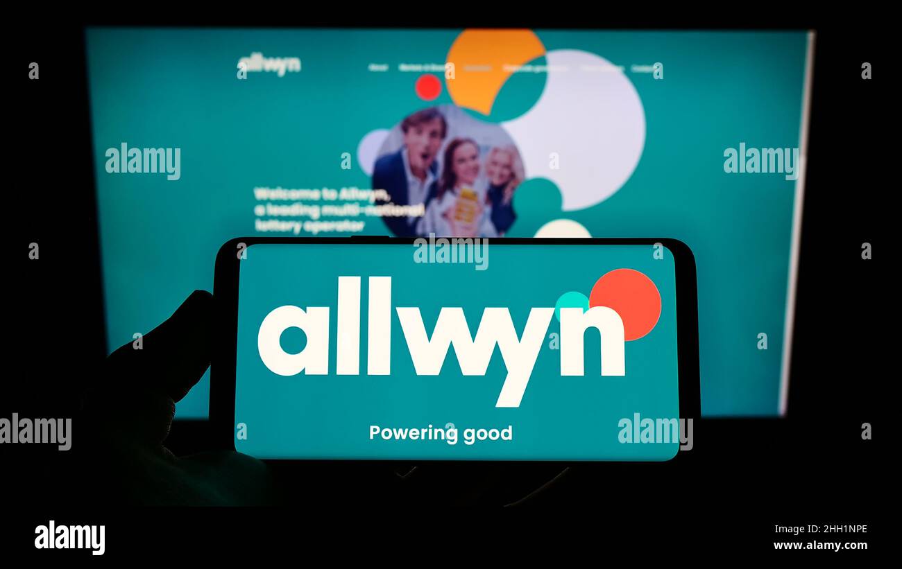 Person holding mobile phone with logo of company SAZKA Entertainment AG (Allwyn) on screen in front of business web page. Focus on phone display. Stock Photo