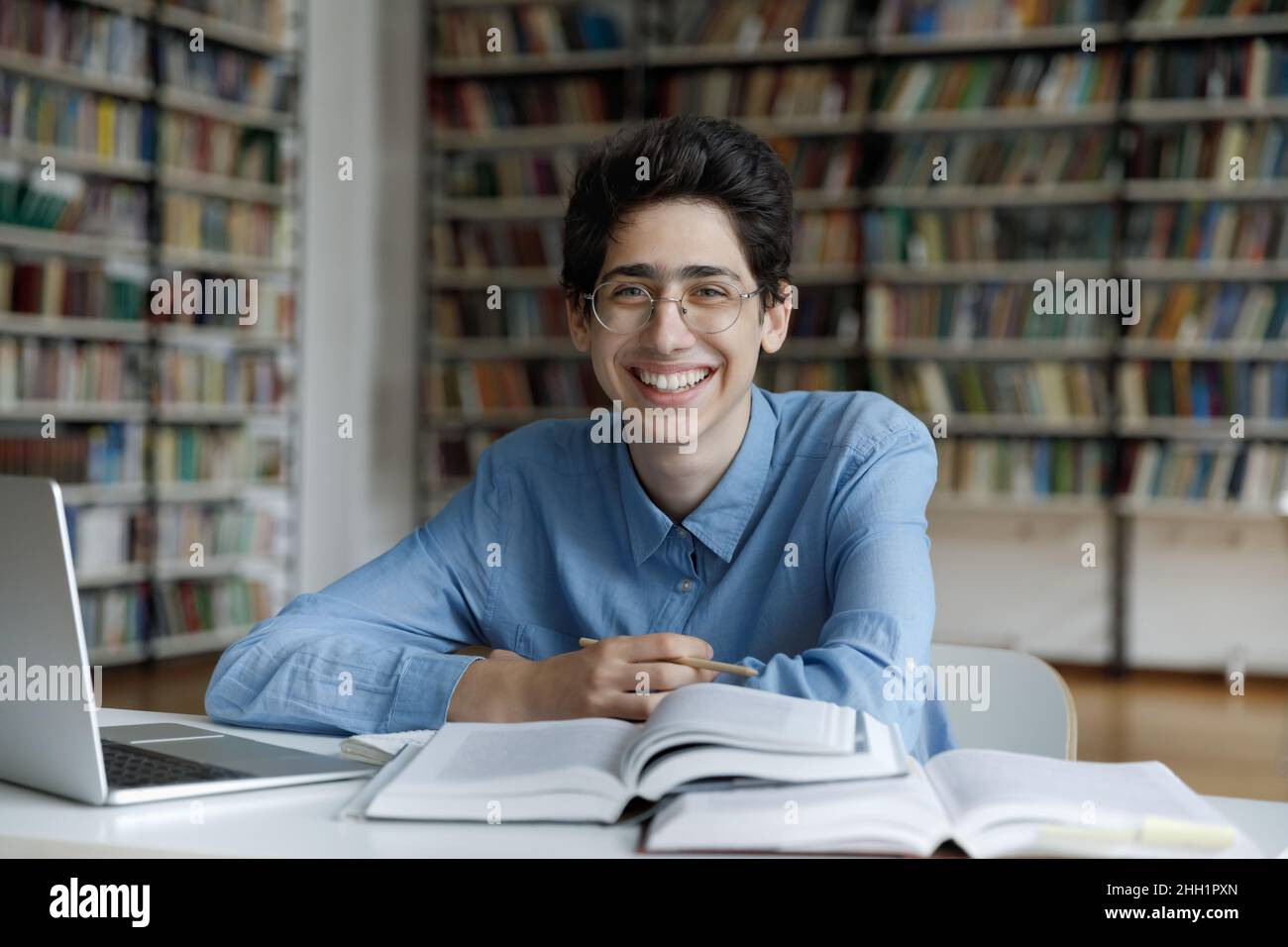 Happy fresh student guy in glasses writing essay in library Stock Photo