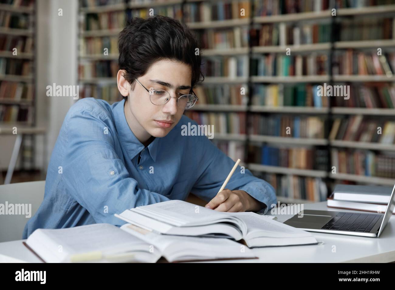 Serious high school pupil working on graduation project in library ...