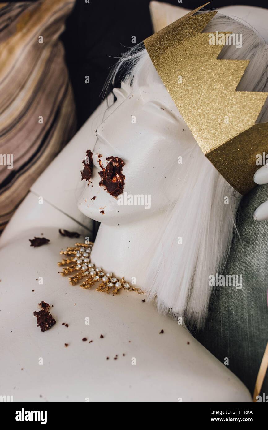 mannequin bust with gold crown and necklace with chocolate cake smeared on face Stock Photo