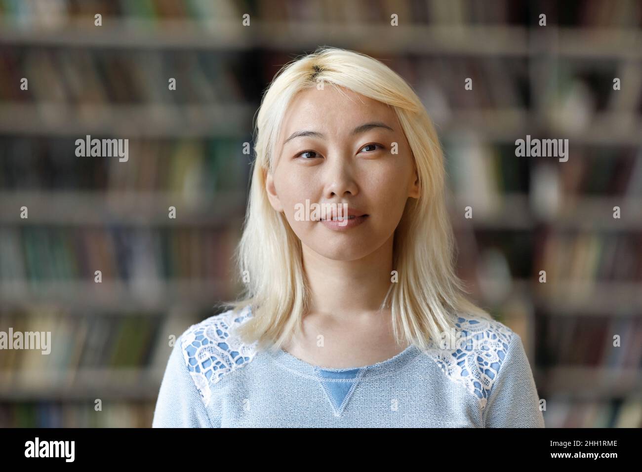 Pensive pretty Asian blonde student girl posing in university library Stock Photo