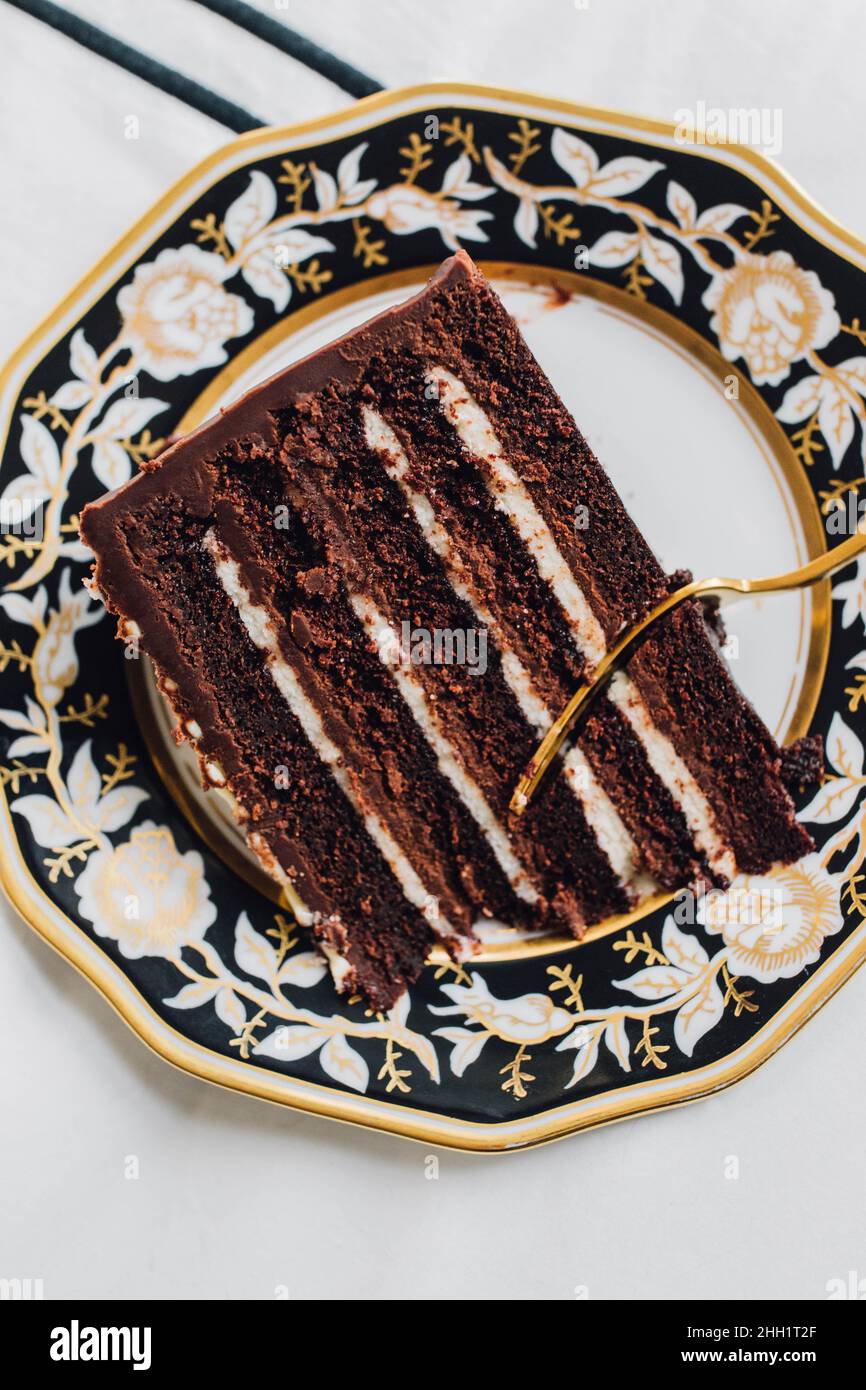 Devil's Food chocolate layer cake on black white gold plate with gold fork Stock Photo