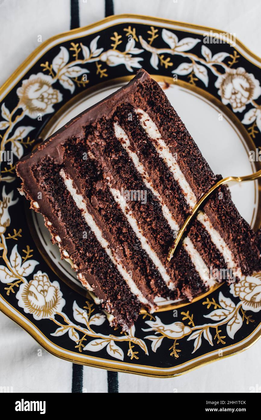 Devil's Food chocolate layer cake on black white gold plate with gold fork Stock Photo