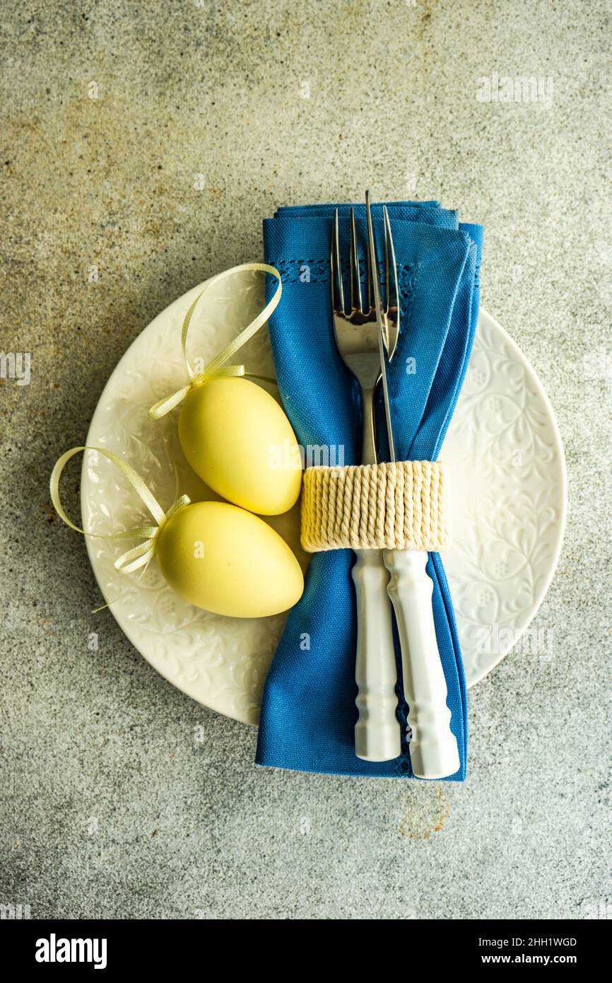 Festive table setting for holiday Easter dinner with yellow eggs and blue napkin Stock Photo