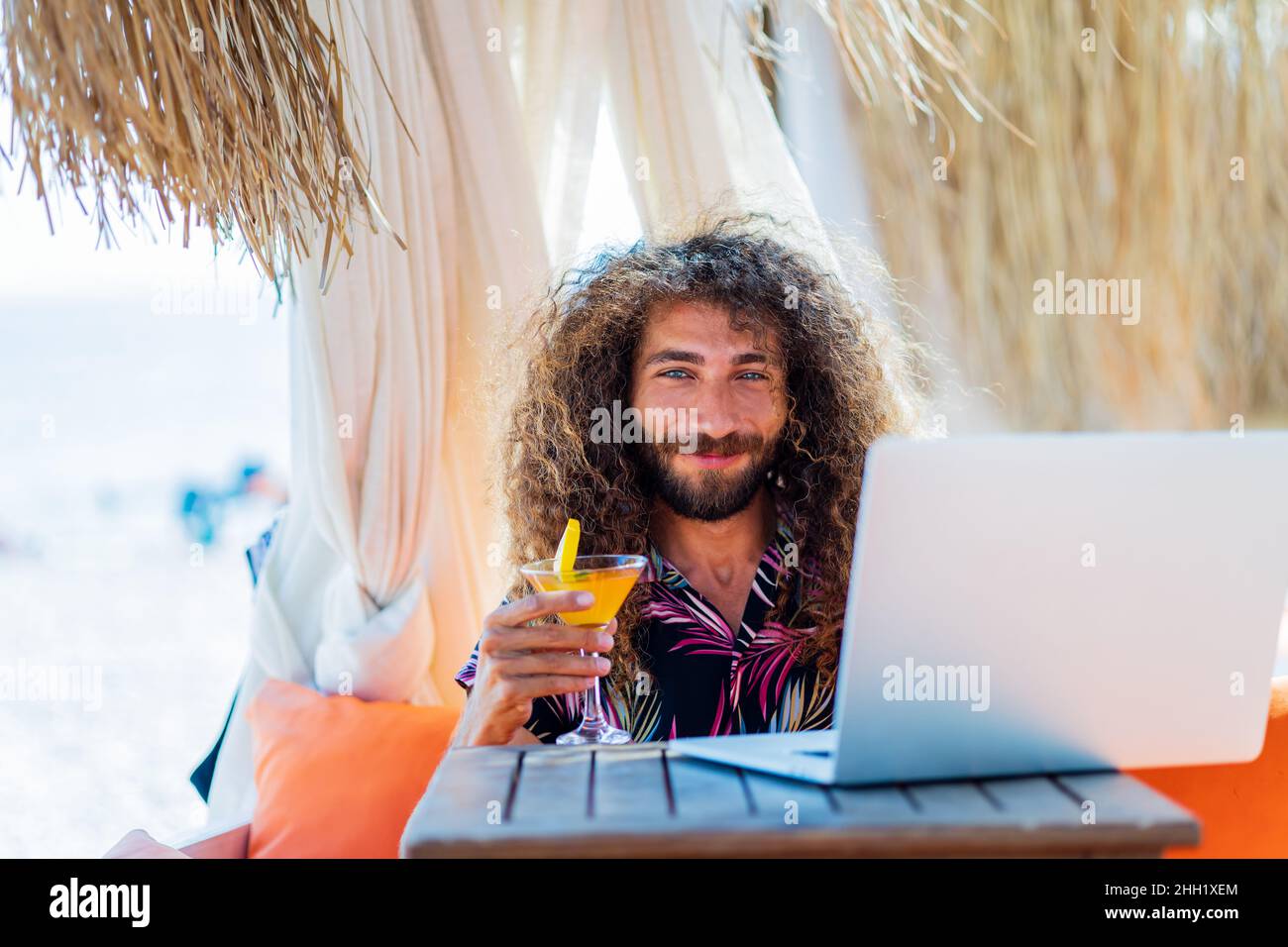 https://c8.alamy.com/comp/2HH1XEM/long-curly-haired-man-sitting-in-beach-and-working-laptop-vacation-2HH1XEM.jpg