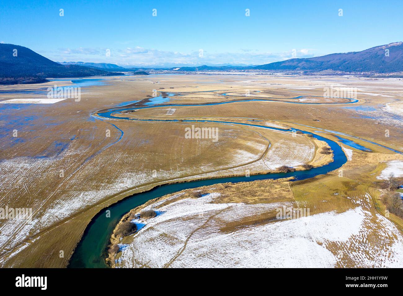 Top aerial view of tributary that flows into Cerknica Lake, beautiful view over the frozen intermittent lake and mountains, taken by drone, Slovenia Stock Photo