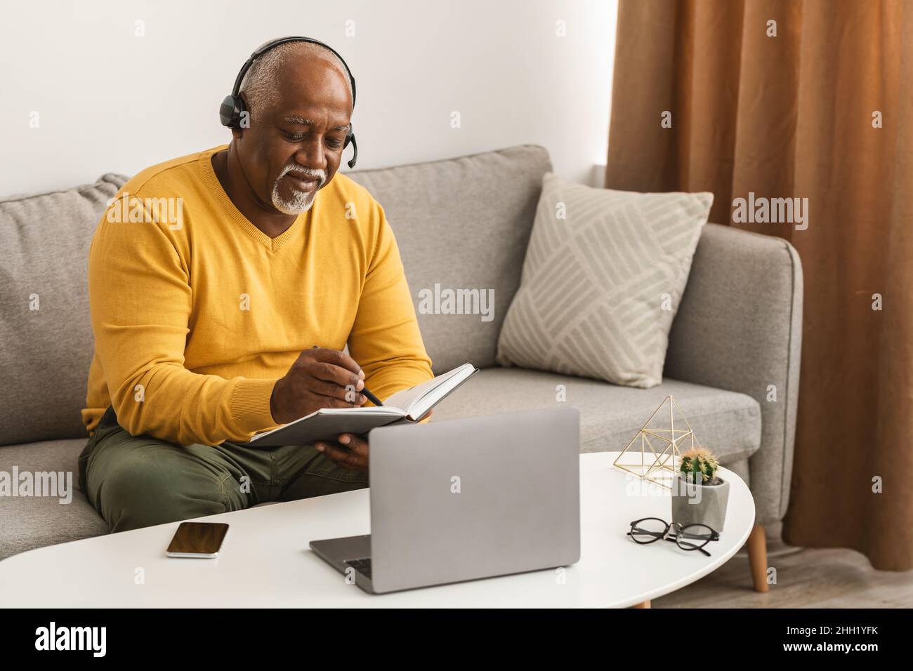 Mature Black Freelancer Man Using Laptop Taking Notes At Home Stock Photo