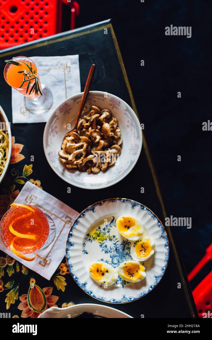 top down view of table with colorful meal eggs, mushrooms, cocktail on high contrast black background with red accents Stock Photo