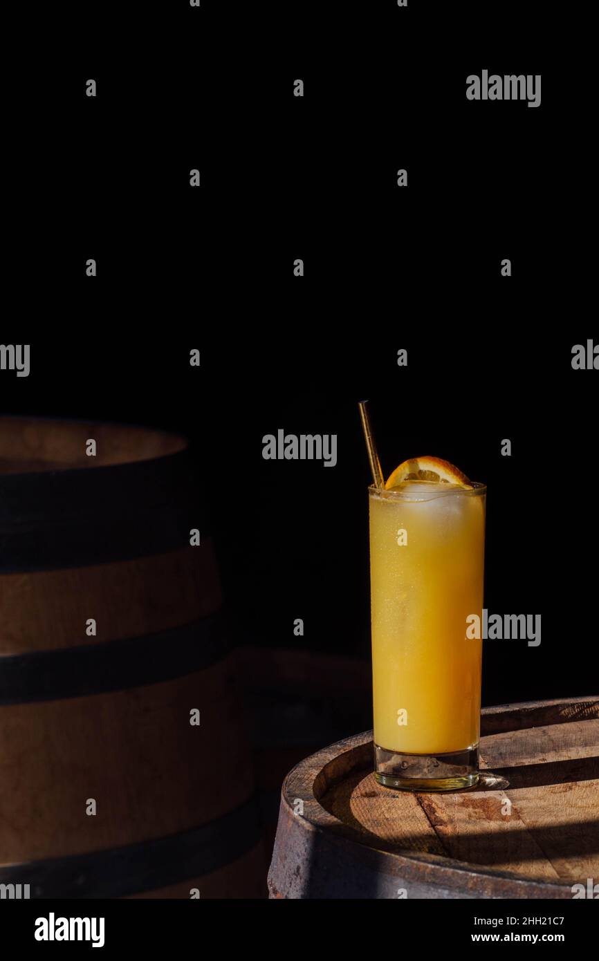 orange juice drink in tall glass with gold straw, sitting on whiskey