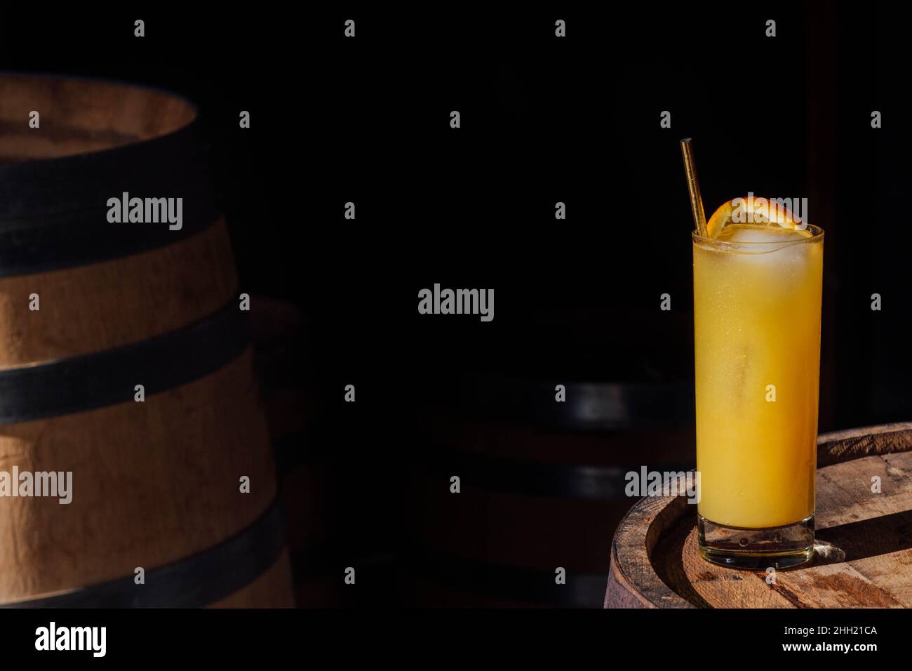 orange juice drink in tall glass with gold straw, sitting on whiskey