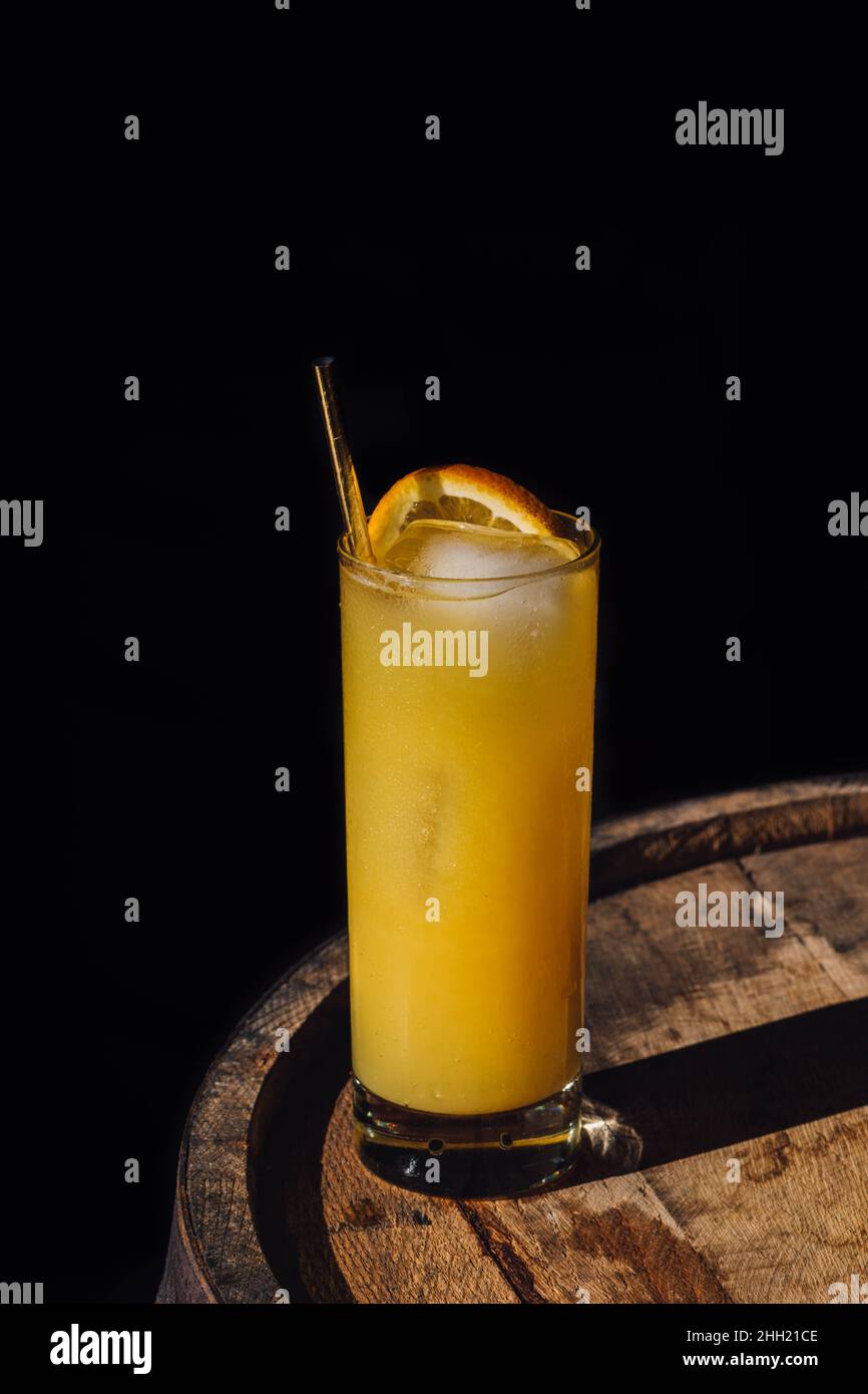 orange juice drink in tall glass with gold straw, sitting on whiskey